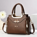 Vintage brown trapezoid handbag with swan metal ornament and tassel on white pedestal - L24 W12 H20cm / Coffee