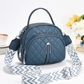 Navy quilted crossbody bag with wide patterned strap and leather texture on white background - Blue