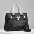 Close-up of black snakeskin embossed handbag with gold padlock and trapezoidal structure - Black