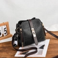 Black vintage square bucket bag with brown leather strap and metal lock on wooden table - Black