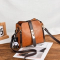 Sac seau en cuir marron avec fermoir doré et charme d'ours sur table en bois sombre - Jaune Terre