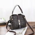 Dark brown vintage bucket bag with monogram print and a bear charm on wooden table - LAD Coffee Color