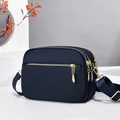 Detail of dark blue nylon crossbody bag featuring three main zipper compartments and gold hardware - Blue (Solid Color)