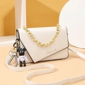 Creamy white crossbody bag with gold chain strap and cute bear charm in minimalist setting - Off White