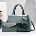 Detail view of dark green textured handbag with pompom charm and matching clutch bag - Green