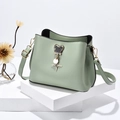 Bolso tipo cubo verde menta con colgante metálico sobre un soporte geométrico - Verde