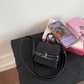 Vista detallada del mini bolso negro con hebilla decorativa sobre superficie de piel fina - Negro