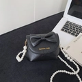 Mini black crossbody bag with white pearl strap and 3D bow on a minimalist desk - Black