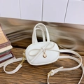 White mini kids crossbody bag with bow and gold heart pendant on a wooden table - White