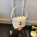 Detail of a mini beige woven bucket bag with silver lock and leather handle shown held by hand - White Naked Bag