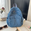 Vue détaillée d'un sac à dos en denim bleu avec poignée violette sur un bureau blanc - Bleu clair