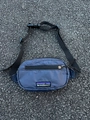 Detail einer dunkelblauen Kinder-Brusttasche aus Ripstop-Nylon auf rauem Asphalt - Schwarz und Grau