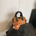Détail d'un sac Boston marron à motif lychee avec bordure noire et breloque ours en peluche - Pendentif Ours Cœur / Marron