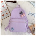 Detail of purple nylon school bag with plaid bow and floral charms on a cozy bed - Purple