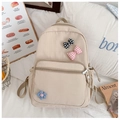 Detailopname van een beige schoolrugzak met geruite strik en bloemenpatches op een bureau - Khaki