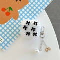 Custodia AirPods glitterata con fiocco nero e ciondolo di perle su sfondo decorativo - Nero / Gen 1/2