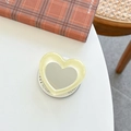 Close-up of heart-shaped mirror phone grip with glitter resin frame on a white desk - Pale Yellow