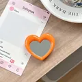 Detail van hartvormige oranje telefoonhouder met spiegel op een houten tafelblad - Oranje