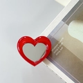 Macro shot of red heart phone grip mirror showing glossy finish on grey desk - Red