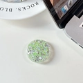 Close-up of a circular phone grip with green glitter sequins on a white desk - Glue Grip - Starry Sequins - Green