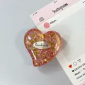 Dettaglio di un supporto per telefono a cuore con glitter rosa, oro e etichetta handmade - Stile 12