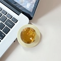 Close-up of a premium amber gemstone phone grip on a white desk next to a laptop - Yellow