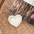 Detail shot of heart-shaped laser phone grip with mirror finish on a vintage book - Adhesive Heart Mirror - Tin Foil Texture