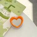 Macro view of orange heart-shaped phone grip with built-in mirror and avocado decor - Orange
