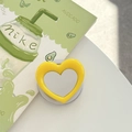 Detailed view of yellow heart-shaped phone grip with circular mirror on a desk - Yellow