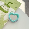 Macro shot of mint green heart-shaped phone grip with built-in makeup mirror on white desk - Dark Green