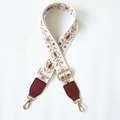 Close-up of ethnic embroidered bag strap with gold metal buckles and red leather details - White Floral Plant + Wine Red