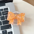Dettaglio del supporto per telefono a fiocco arancione con glitter e base pieghevole - Arancione