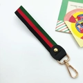 Macro shot of striped woven wristlet strap with gold metal lobster clasp and leather trim - Green-Red-Black