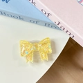 Macro detail of a bow-shaped phone grip made of transparent resin with yellow sequins - Yellow Sugar Heart (Large Bow Stand)