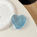 Macro shot of a transparent blue heart-shaped grip with silver glitter on white surface - Large Crooked Heart - Glitter Dots / Transparent Blue