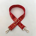 Close-up of red wide adjustable bag strap with golden geometric patterns and metal hooks - Red