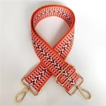 Detail eines lebhaften orangefarbenen Stickereitaschenriemens mit Gold-Karabinern und Mustern - Orange
