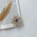Dettaglio della spilla a fiocco di neve con gemma blu e perle su un libro d'epoca - Blu