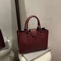 Sac cabas élégant en cuir bordeaux avec finitions dorées sur un support décoratif - Rouge