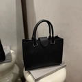 Sac fourre-tout noir en cuir à motif litchi avec détails dorés sur un socle minimaliste - Noir