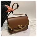 Detail der karamellbraunen Ledertasche mit Goldkette und Metalllogo-Verschluss nah - Braun