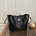 Bolso tipo cubo de cuero sintético negro con cierre dorado sobre mesa de madera - Negro