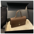 Dettaglio borsa a mano in pelle marrone con chiusura dorata e confezione regalo di lusso - caffè