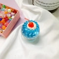 Makroaufnahme einer blauen Jelly-Kirsch-Cupcake-Handyhalterung auf weißem Stoff - Cremige Kirsche-Blau