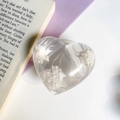 Makroansicht der klaren Herz-Handyhalterung mit weißem Glitzer auf einem Buchhintergrund - Transparente Wolke Herz Halterung