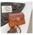 Detail of caramel brown croc-embossed handbag styled on grey fabric with elegant props - Brown