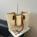 Off-white woven tote bag with brown leather handles and zipper closure on books - White