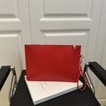Elegante pochette a busta rossa con cerniera dorata e cinturino su sfondo di un libro - Rosso
