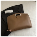 Detail of a brown leather trapezoid handbag with silver metal handles on a white surface - Brown