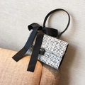 Elegant tweed handbag with black satin bow and leather handle on a textured sofa - White